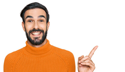 Young hispanic man wearing casual clothes with a big smile on face, pointing with hand and finger to the side looking at the camera.