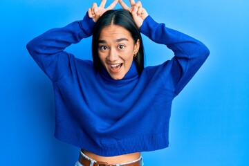 Poster - Young asian woman wearing casual winter sweater posing funny and crazy with fingers on head as bunny ears, smiling cheerful