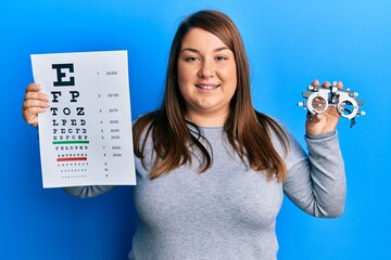 Wall Mural - Beautiful brunette plus size woman holding optometry glasses and eyesight test smiling with a happy and cool smile on face. showing teeth.