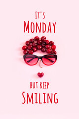 Wall Mural - Positive motivational quote. It's Monday but keep smiling text and abstract image young woman from sweet cherry and glasses on pink background. Concept inspirational quote of the day