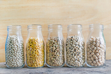 Five types of cereal and grain seeds in glass bottle consisnted of white bean, soybean, lentil, black eye pea and chick pea, on wooden background