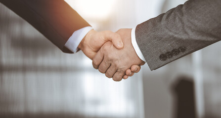 Business people standing and shaking hands in sunny office, close-up. Handshake and marketing