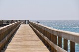 Fototapeta Morze - Single seagull sitting on the handrail of a pier in Swakopmund (Namibia) on a sunny day with light blue sky and no clouds
