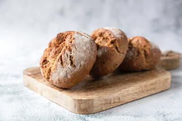 Round fresh buns made from whole grain or rye flour lie on a wooden board. Traditional baked goods in Europe. Place for your text. Bakery, production of bakery products