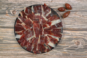 Wall Mural - Portion of 100% acorn-fed Iberian ham Dehesa de Extremadura decorated with acorns on wooden background