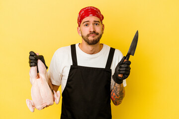 Wall Mural - Young tattooed batcher caucasian man holding a chicken isolated on yellow background