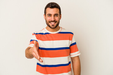 Young caucasian man isolated on white background stretching hand at camera in greeting gesture.