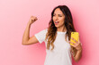 © Asier - Young mexican woman holding a mobile phone isolated on pink background raising fist after a victory, winner concept.
