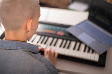 The girl plays the electric piano and watches the video. A woman is learning to play the synthesizer on a laptop