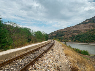 Old mountain railroad track leading between forest and lake.