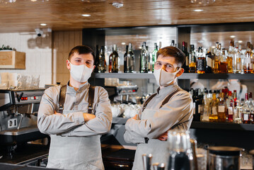 Two stylish bartenders in masks and uniforms during the pandemic, stand behind the bar. The work of restaurants and cafes during the pandemic.