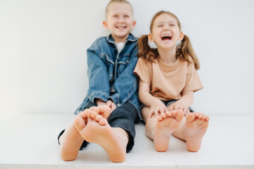 Cheerful little siblings sitting on a table with bare feet. Both laughing. Faces blurred, focus on their feet.