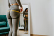 © shevtsovy - Fitness Woman Measuring butt With Tape at home. strong buttocks concept. Beautiful woman checking success of weight loss program and measuring butt and hips in front of mirror in living room.