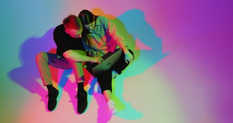 Modern couple, coworkers use laptop computer working. Remote work. Colourful neon studio light. Top view