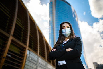 Wall Mural - Confident young female manager outdoor in a modern urban setting and wearing a protective mask against covid 19 coronavirus pandemic