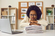 © Studio Romantic - Lazy displeased fatigue young frowning african american woman worker employee keeping chin on paper stack folder pile sitting at table in office. Work overtime load, lots of paperwork concept