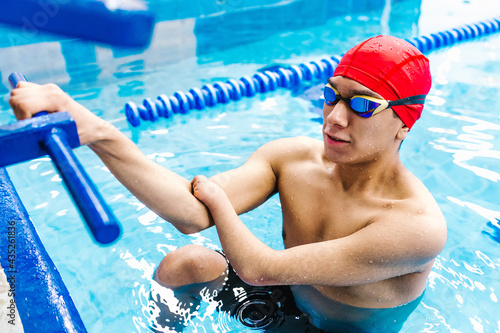 disabled latin man paralympic athlete wearing cap and goggles in a swimming training  holding On Starting Block In the Pool in disability concept with hand hypoplasia