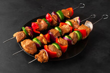 Raw skewers of meat. Barbecue marinated pork meat with vegetables and spices on black background