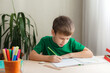 © OlgaKhorkova - 7 years old child boy doing lessons sitting at desk in his room. Kid writing homework in notebook