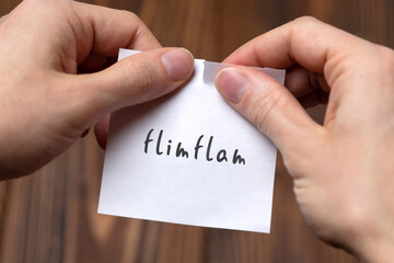 Hands tearing off paper with inscription flimflam