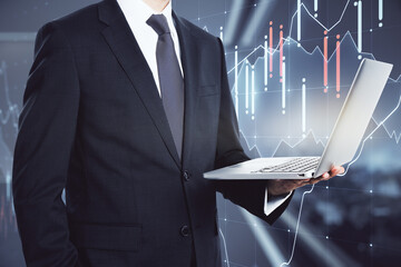 Wall Mural - Businessman holding a laptop closeup in an office corridor with trading chart in the background, market analysis concept