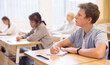 © JackF - Smart teenager studying in classroom, listening to lecturer and writing in notebook..