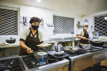 Vertical shot of two Hispanic women cooking chicken with mushroom sauce and French fries