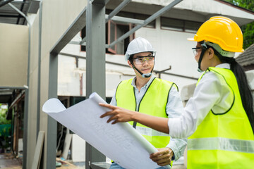 Asian male engineer explaining job on blueprint to female worker.