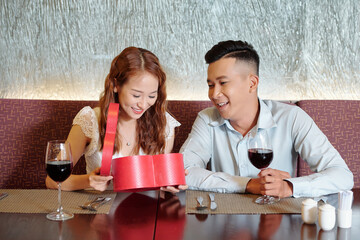 Wall Mural - Happy pretty young woman opening heart shape giftbox from her boyfriend when they are having date in restaurant