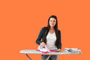 Beautiful young woman ironing clothes on color background