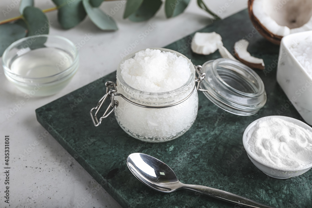 Jar of coconut body scrub and ingredients on light background