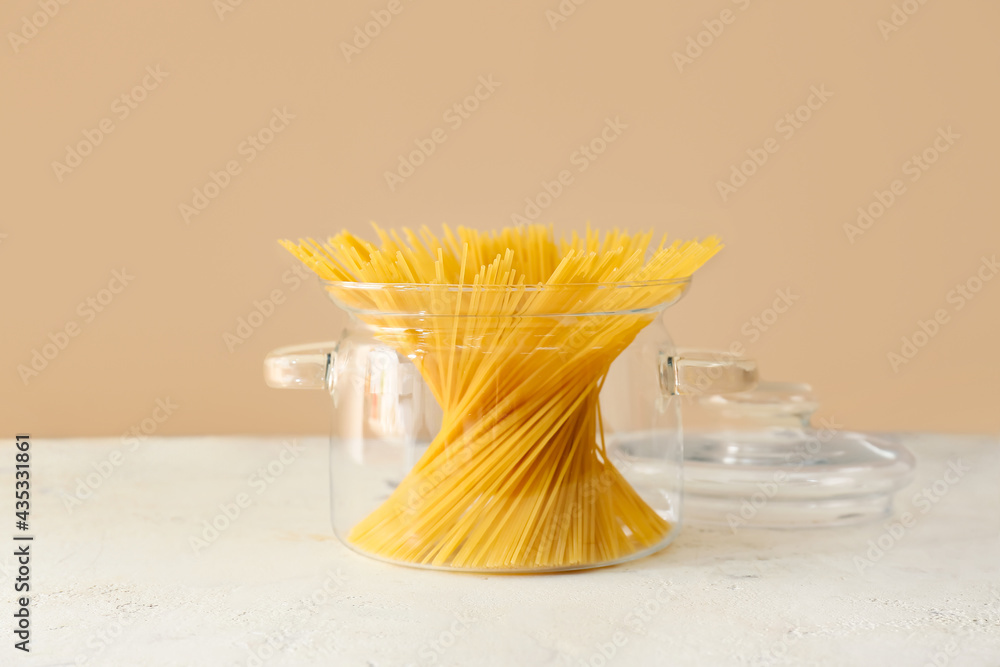 Stylish cooking pot with uncooked pasta on color background