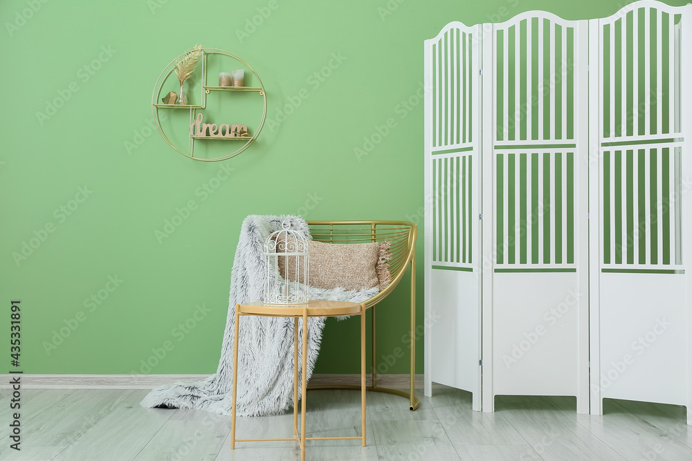 Modern armchair with table and folding screen near color wall