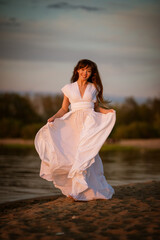 Wall Mural - beautiful, young brunette woman in a white flowing dress on the sandy beach in the evening. full-length portrait in natural light.