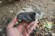 A hand is holding a specimen of a piece of Magnetite mineral rock.   iron ore