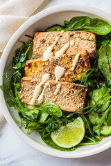 Wall Mural - Fried tofu with green salad and tahini dressing in white bowl. Asian cuisine, vegan food concept.