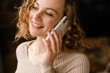 Wall Mural - Young blonde woman smiling while talking on mobile phone at home