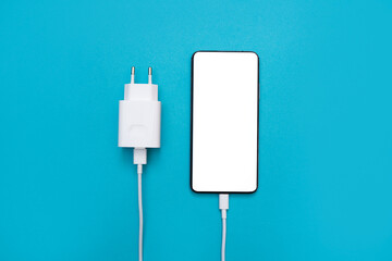 Smartphone with white phone screen and power supply, phone charger on a blue background. USB cable for wired charging of the phone battery. Flat lay, top view, copy space for text