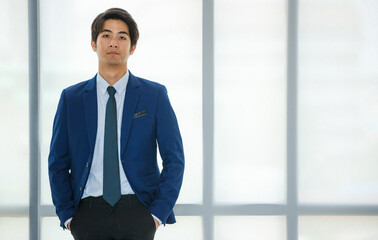 Portrait 20s handsome young Asian confident rich businessman wearing formal suit with necktie,  standing next to window with hands put in pocket pants,  looking at camera with profession, success.