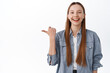 © Cookie Studio - Hey check this out, logo here. Smiling pretty teenage girl with long healthy hair smiling, pointing thumb aside at promo text, showing advertisement copy space, white background