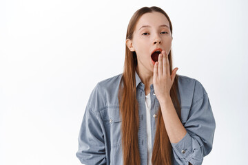 Wall Mural - Tired or bored teenage girl student, yawning and looking indifferent sleepy, standing in casual clothes against white background