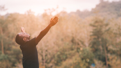 Freedom african man is relaxing in green nature with squint eyes and raised up to sky arms at sunny summer day. Emotion feel good and travel adventure concept