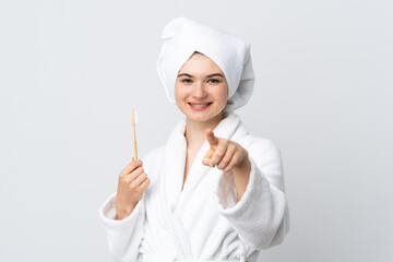 Young woman in a bathrobe holding toothbrush points finger at you with a confident expression