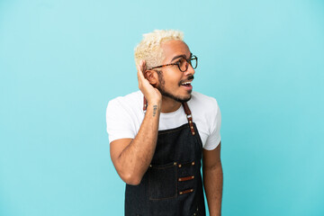 Sticker - Restaurant Colombian waiter man isolated on blue background listening to something by putting hand on the ear