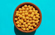 Cheese coated salted peanuts in a brown bowl on bluea background. Fried peanut grains with a coating of savory spices. Top view.