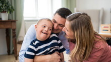 Cheerful Down Syndrome Boy With Parents Indoors At Home Hugging.