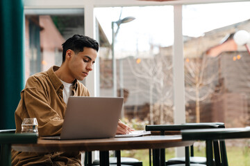 Wall Mural - Young hispanic man student sitting at the cafe table indoors