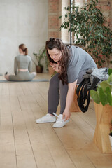 Wall Mural - Disable girl with Down syndrome in sportswear doing her sports-shoes while sitting on bench in gym