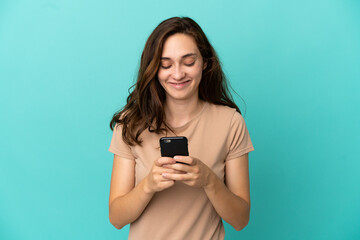 Young caucasian woman isolated on blue background sending a message or email with the mobile