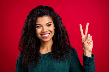 Photo of pretty charming dark skin lady wear green sweater showing v-sign smiling isolated red color background